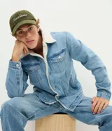 Chaqueta de jean azul con forro interior de sherpa en el cuello y cuerpo. Presenta cierre frontal con botones metálicos, bolsillos frontales con solapa y bolsillos laterales funcionales.