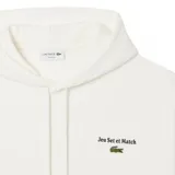 Canguro Lacoste de color blanco, con capucha ajustable mediante cordones, bolsillo frontal tipo canguro y puños y ruedo acanalados. Presenta un pequeño bordado en el pecho con el logo de la marca y la frase 'Jeu Set et Match'.