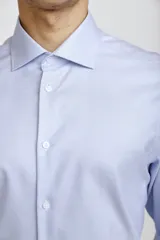 Camisa de vestir blanca de corte clásico, con cuello rígido, cierre frontal de botones y mangas largas con puños abotonados.