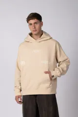 Buzo canguro color beige con capucha, bolsillo frontal tipo canguro y estampado gráfico sutil en el pecho. Presenta un diseño oversize con puños y ruedo acanalados.