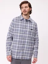 Camisa de manga larga con estampado de cuadros en tonos blanco, gris y azul. Presenta cuello clásico, cierre frontal con botones y un pequeño parche con logo en el pecho.