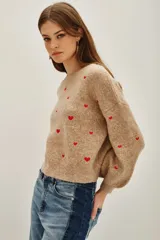 Sweater de punto color beige melange con bordado de pequeños corazones rojos distribuidos por toda la prenda. Posee cuello redondo, mangas largas y terminaciones acanaladas en puños y ruedo.