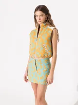 Chaleco corto color naranja con estampado de flores turquesa, cuello alto, cierre frontal y bolsillos con cierre.