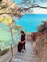 Vestido largo tejido de algodón color negro, sin mangas, con cuello redondo y tajos laterales. Presenta dos bolsillos de cuero color marrón en el frente.