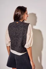 Chaleco sin mangas de corte al cuerpo, color negro con bordados florales en hilo contrastante. Presenta un diseño abierto con terminaciones reforzadas.