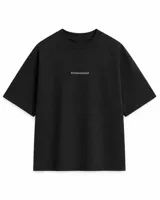 Remera de algodón premium color negro, con corte boxy, cuello redondo y mangas cortas amplias que llegan hasta el codo. Cuenta con un pequeño texto estampado en el centro del pecho.
