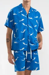 Short de algodón azul con estampado de sirenas blancas, corte relajado y largo hasta la rodilla. Tiene cintura elástica con cordón ajustable, dos bolsillos laterales y un bolsillo trasero tipo parche.