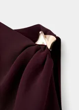 Blusa sin mangas de color marrón oscuro, con diseño asimétrico y cuello redondo. Presenta un detalle metálico en uno de los tirantes, fruncido lateral y un corte entallado al cuerpo.