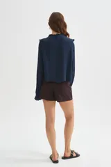 Blusa blanca de viscosa con cuello a la base, mangas largas abullonadas con puños ajustados, detalles de volados, encaje y botones frontales.