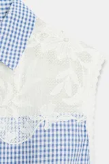 Blusa sin mangas con estampado de cuadros vichy en color azul y blanco, con cuello camisero y detalle de encaje floral en la parte superior delantera y trasera. Presenta cierre frontal con botones y un ligero volante en el ruedo.
