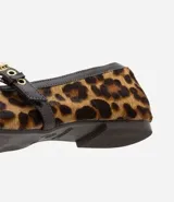 Zapatilla estilo Mary Jane de cuero con estampado animal print de leopardo. Presenta una tira superior ajustable con hebilla metálica dorada y detalles de ribete en color marrón oscuro.