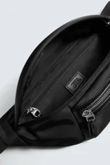 Riñonera negra de tejido técnico con múltiples compartimentos con cierre de cremallera, incluyendo uno frontal y uno interior. Posee asa ajustable con hebilla metálica de liberación rápida.