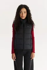 Chaleco acolchado negro con cuello alto y cierre frontal con cremallera. Tiene un logo pequeño de la marca en el pecho.