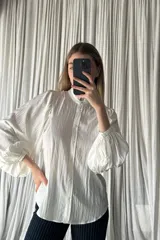 Camisa negra de corte clásico con cuello alto tipo mao con volados, cierre frontal de botones y mangas largas abullonadas con puños ajustados.