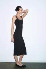 Vestido midi negro, entallado, con escote en pico y tirantes anchos. Presenta detalle de costuras verticales a tono que simulan entredós.