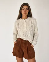 Buzo de punto crudo con trama calada de diseño geométrico, cuello redondo acanalado, cierre frontal parcial con botones y mangas largas con puños ajustados.