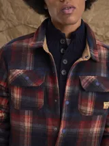 Sobrecamisa de tejido polar con estampado abstracto en tonos rojizos y azul marino. Presenta cuello clásico, cierre frontal con botones a presión, dos bolsillos frontales con solapa en el pecho y un parche decorativo.