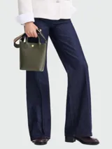 Bolso tipo tote en tamaño XS, confeccionado en cuero de color verde oliva. Presenta una estructura rígida, doble asa corta de mano y una correa ajustable y extraíble en tono beige. Incluye un cierre de botón a presión con el logo de la marca en el centro.