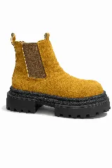 Botas tipo chelsea de gamuza color mostaza, con paneles elásticos laterales marrones y suela track de goma negra con plataforma dentada.