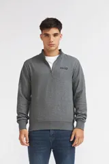 Buzo Quiksilver modelo Kian para hombre, color gris melange, con cuello alto y cierre frontal parcial de ¼. Presenta mangas largas, puños y dobladillo acanalados, y un pequeño parche rectangular con el logo de la marca en el pecho.