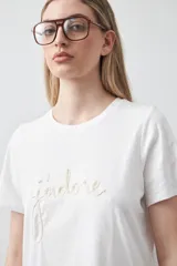Remera de manga corta confeccionada en algodón de tacto suave, con cuello redondo y bordado frontal en relieve con la palabra 'J'adore' en tipografía cursiva.