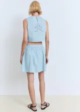 Falda corta evasé de algodón color celeste, con diseño fluido, detalles bordados y bajo festoneado. Cuenta con cierre de cremallera lateral.
