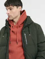 Campera puffer de corte largo, color verde militar, con capucha fija, cierre frontal y puños elásticos internos.