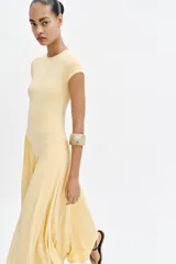 Vestido largo color amarillo pastel, confeccionado con mezcla de viscosa, con cuello redondo, manga corta y bajo asimétrico fruncido con volumen.