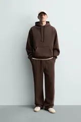 Pantalón jogger de corte relajado y pernera ancha, confeccionado en tejido de algodón con interior perchado. Presenta cintura elástica con cordón interior, bolsillos laterales y un bolsillo trasero de plastrón.