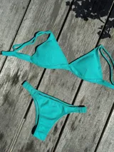 Conjunto de bikini color turquesa con textura acanalada. El top es de estilo triangular con breteles regulables y cierre de gancho en la espalda. La bombacha es de corte vedetina con laterales fruncidos elásticos.
