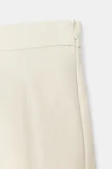 Falda midi de tiro medio y efecto piel en color marfil, con diseño acampanado y cierre lateral con cremallera oculta. Incluye un cinturón fino a juego con hebilla metálica ovalada.