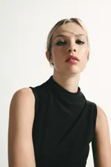 Vestido midi negro con cuello subido y diseño sin mangas (sisa). Presenta un elegante detalle de tejido drapeado en el lateral y cierre trasero con cremallera oculta.