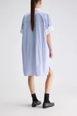 Vestido camisero midi de calce relajado a cuadros en tonos verde y negro, confeccionado en algodón liviano. Presenta cuello clásico en contraste de color blanco, cartera frontal oculta con botones y mangas cortas con vuelta.