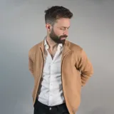 Campera tejida color marrón claro con cierre frontal, cuello alto y mangas largas con puños acanalados.