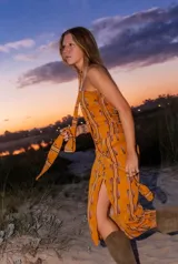 Vestido midi strapless color dorado con estampado de hojas y rayas verticales. Incluye una tira de tela que se ata al cuello.