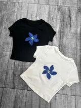 Remera de algodón con estampado de una flor azul de cinco pétalos con centro amarillo. Disponible en blanco y negro.