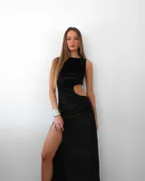 Vestido largo negro de terciopelo, con cuello redondo, sin mangas, abertura lateral en la pierna y recorte en la cintura.