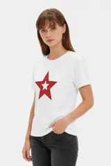 Remera blanca de manga corta y cuello redondo, confeccionada en algodón, con un diseño holgado y estampado frontal de estrella roja con textura y detalles de estrellas pequeñas.