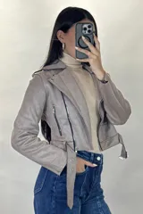 Chaqueta corta tipo biker confeccionada en gamuza color beige, con cierre frontal cruzado, solapas amplias, bolsillos con cierre y cinturón ajustable en la cintura.