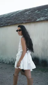 Falda corta de color blanco con tejido bordado y sutil brillo plateado. Presenta un diseño con volado en el ruedo, corte evasé y caída liviana.