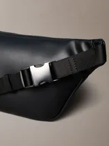 Riñonera Calvin Klein negra de poliuretano, diseño waist bag con cierre de cremallera superior, correa ajustable y monograma CK grabado en la parte delantera.