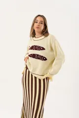 Sweater color manteca de tejido de punto con cuello redondo y ribete marrón. Presenta dos peces marrones tejidos en el frente con detalles bordados a mano.