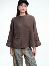 Sweater de tejido de punto color marrón con textura tipo waffle, diseño amplio, hombros caídos y cuello redondo. Presenta un bolsillo frontal aplicado y mangas con puños anchos decorados con botones.