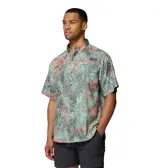 Camisa de manga corta Columbia modelo Super Tamiami, con estampado tropical de hojas en tonos verdes, rosados y naranjas. Presenta cuello abotonado, cierre frontal con botones y bolsillo en el pecho con logo de la marca.