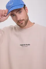 Buzo color beige de manga larga y cuello redondo con logo pequeño en el pecho. Corte relajado y tejido de bucle.