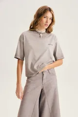 Remera gris de corte relajado, con cuello redondo, mangas cortas y pequeño estampado en el pecho.