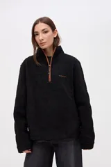 Buzo de sherpa doble faz con textura capitoneada, color negro, con cuello alto y medio cierre frontal en color contraste. Presenta bolsillos laterales y bordado en el pecho.