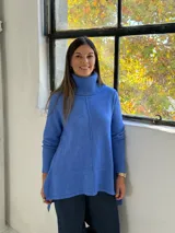 Sweater de punto color azul, con cuello alto acanalado, mangas largas y diseño holgado con costuras verticales decorativas.