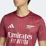 Camiseta de calentamiento Adidas del Arsenal FC, color bordó con estampado de rayas verticales sutiles. Presenta cuello redondo, logo de Adidas y escudo del club en contraste blanco, con tecnología Aeroready para mayor transpirabilidad.