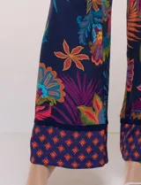 Pantalón pull on largo de caída fluida, cintura alta con pretina trasera elastizada, pierna de corte ancho tipo palazzo y detalle de guarda geométrica sobre el ruedo inferior, con estampado floral multicolor sobre base azul.